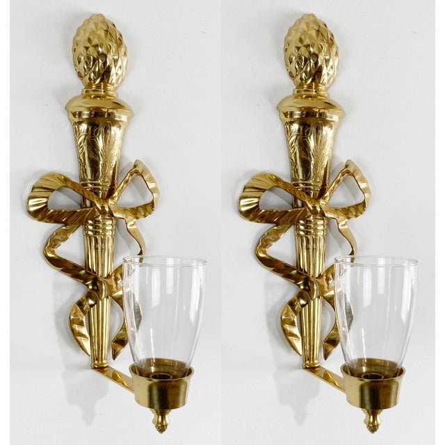 Vintage pair of large classic solid brass French Empire style sconces, each with a ribbon tied torch. The sconces have one...