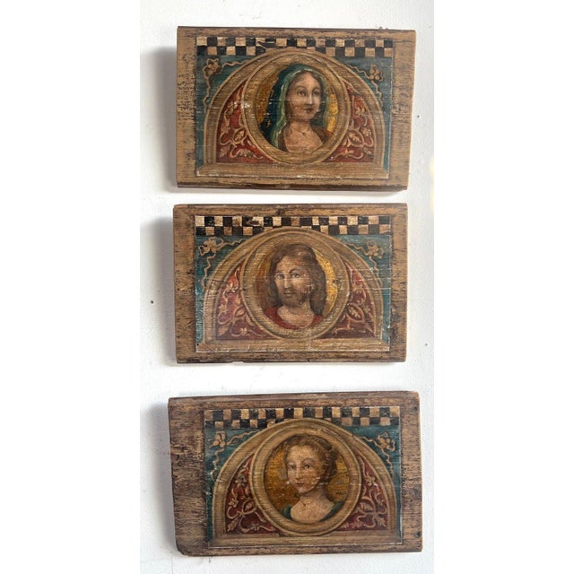 A set of three hand painted wooden plaques, each featuring a religious portrait within a decorative frame. The center...