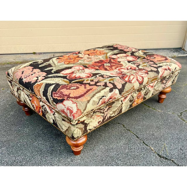 This beautiful unmarked ottoman is in a floral Kilim with brass nailhead trim on turned wooden legs.