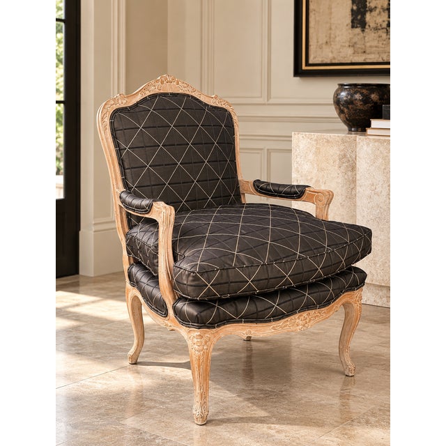 An elegant vintage Louis XV–style bergère armchair featuring a carved exposed wood frame and upholstered seat, back, and...