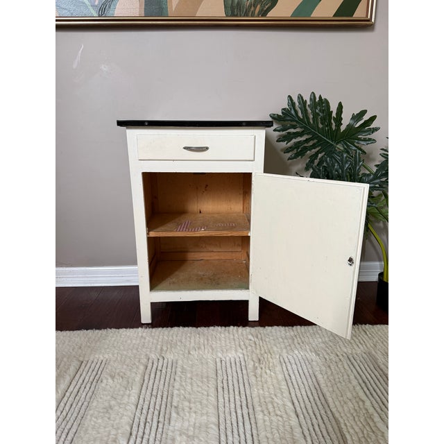 Cute early 1900s antique enamel top small cabinet or tall side table. Features a drawer on top and a spacious cabinet with...