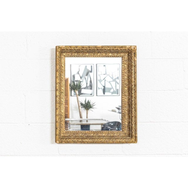 This vintage antique hanging wall mirror has an elegant design with an ornate painted brass-toned wooden outer frame....