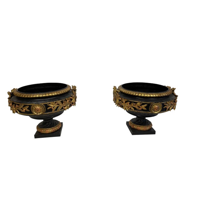 Pair of neoclassical black and gold classical cast iron urns. Spectacular pair with bow, garland and medallion decoration....