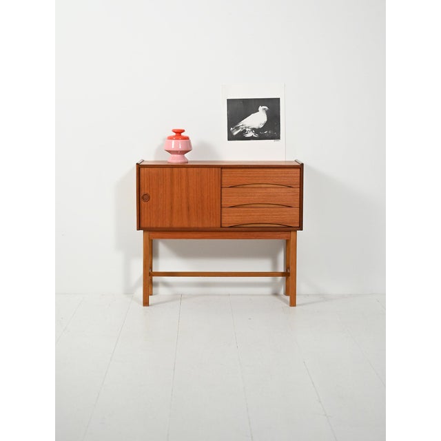 Warm teak, compartment with sliding door and three drawers with half-moon handles. Lightweight structure on a thin-section...