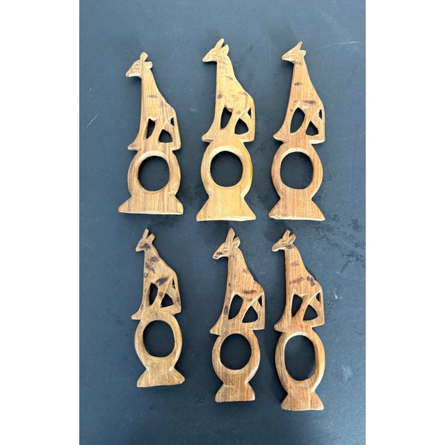 A sculptural set of six hand-carved wooden giraffe napkin rings, featuring a graduated height design that adds visual...