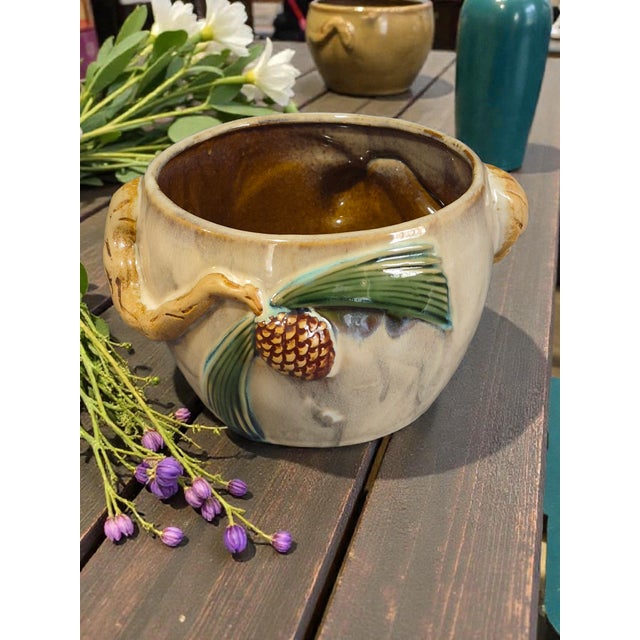 The product is a vintage glazed pottery pine cone jardinière planter, made of clay with a glossy finish. It is in the Arts...