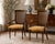 A sophisticated pair of vintage French Regency armchairs featuring elegant cane backs, sculpted walnut-toned frames, and...