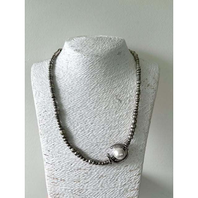 This specific piece is known for its handcrafted aesthetic, featuring a mix of irregular silver-plated beads and a central...