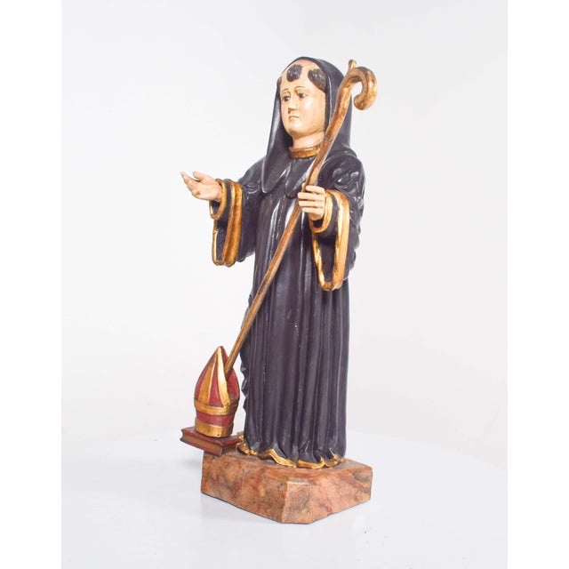 Wooden sculpture representing Saint Benedict. Black habit with staff in hand and at his feet, the skullcap on top of a...
