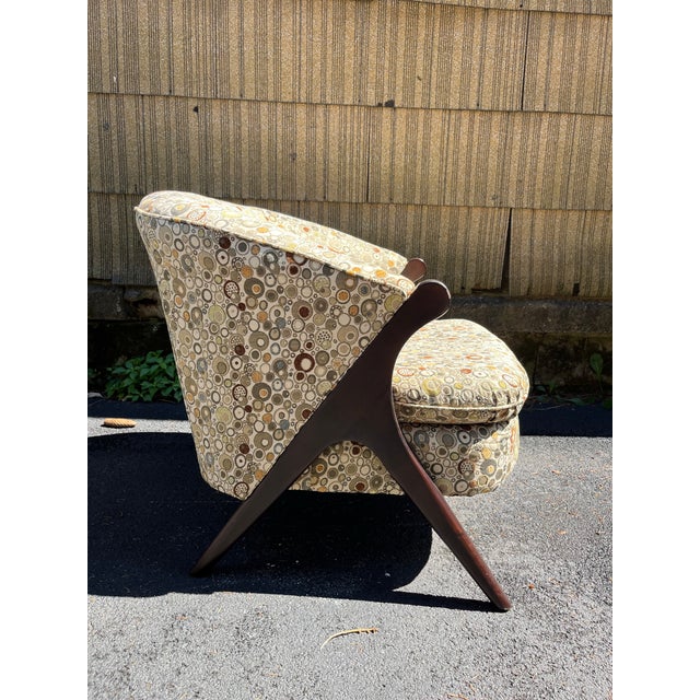 A single mid century style upholstered tub or lounge chair with angled wood legs and arms. Finished with an attached...