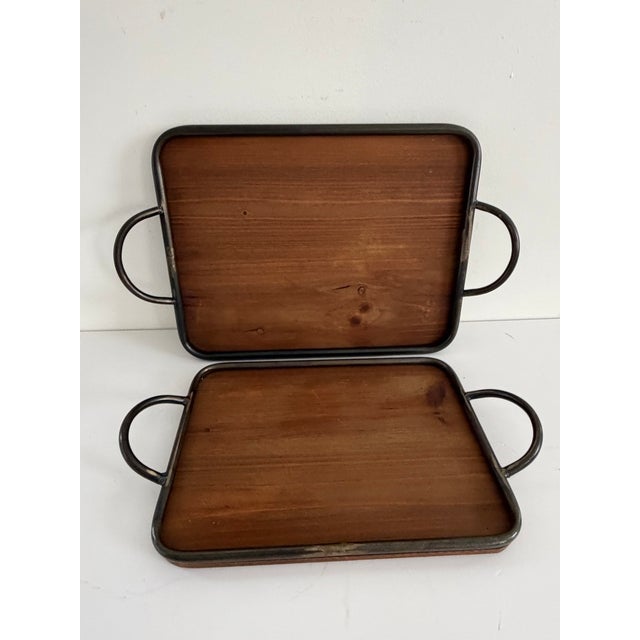 Set of two handmade rectangular serving trays with solid wood bases and hand-forged metal frames and handles. The trays...