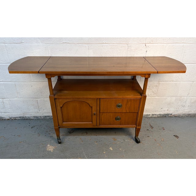 A stylish mid-century modern bar cart crafted in warm walnut with brass casters and matching brass handles. Features a...