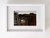 This artwork depicts an interior view of a rustic structure, framed by weathered wooden beams that lead the eye toward a...