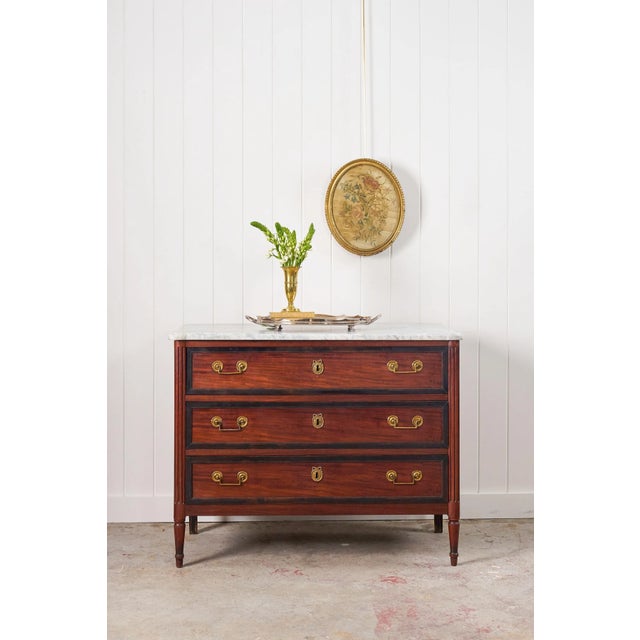 This elegant Louis XVI period French commode, crafted circa 1780, features a white marble top and rich mahogany wood tone....