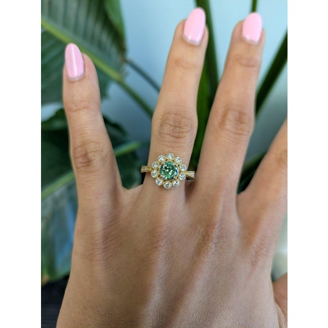 A rare demantoid garnet glows in a vivid, fiery green at the center of this solid 14K yellow gold ring, set in a floral...