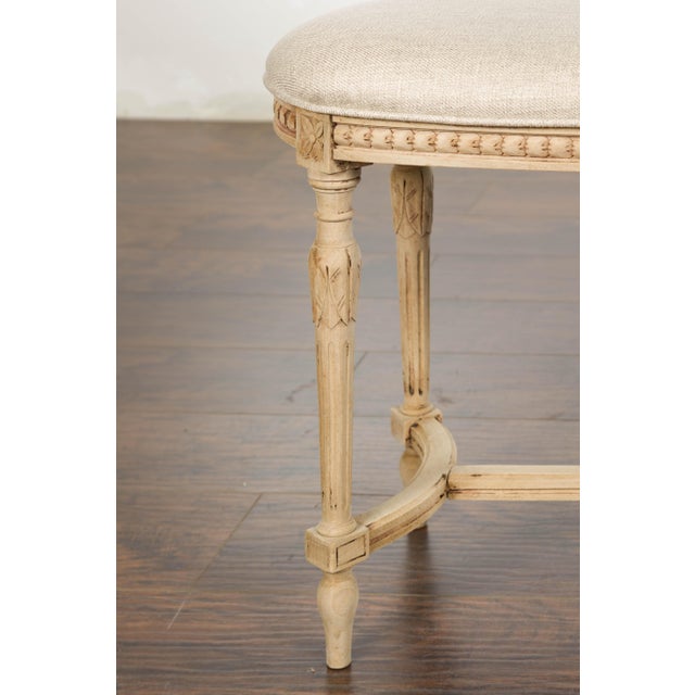 A French Neoclassical style walnut bench from circa 1900 with carved décor, fluted carved legs on arrow feet and cross...