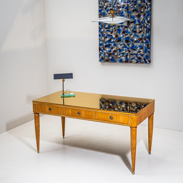 Large desk raised on tapered legs with brass ball feet and three drawers with round pulls. The writing surface is outlined...