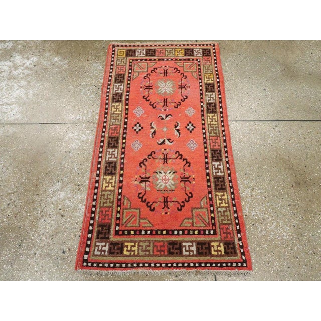 An antique East Turkestan Khotan throw rug. The salmon-pink field of this lively small scatter from the Xinjiang oasis...