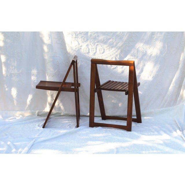 Pair of Midcentury modern folding chairs in a darker stained wood. Aged brass hardware. Stamped on the back. Made in...
