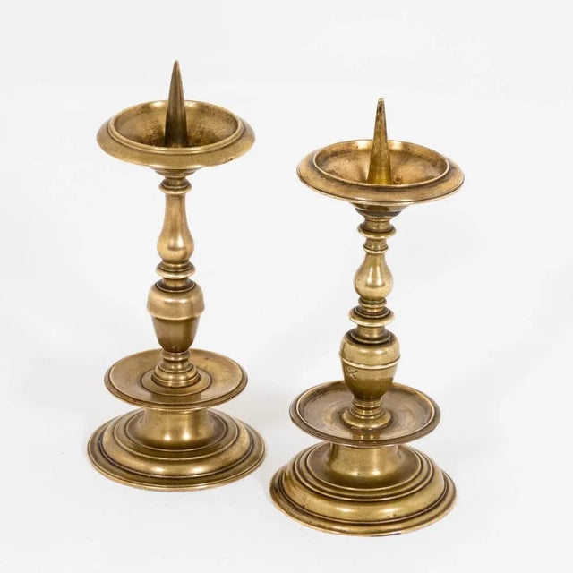 Two brass candlesticks with balustraded shafts and drip trays with spikes. The candlesticks are not identical in their...