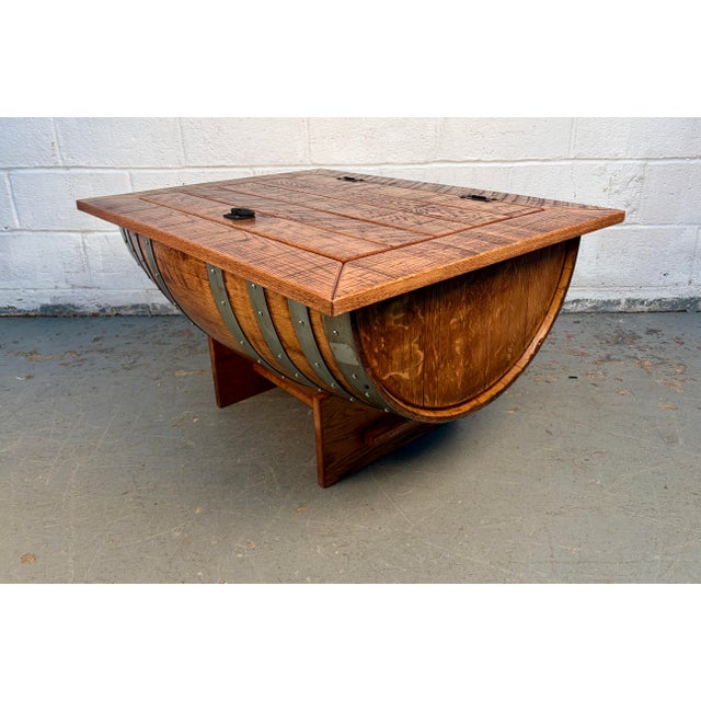 Professionally crafted half barrel table featuring a distressed saw-mark finish, black cast-iron handles, and a lift-up...