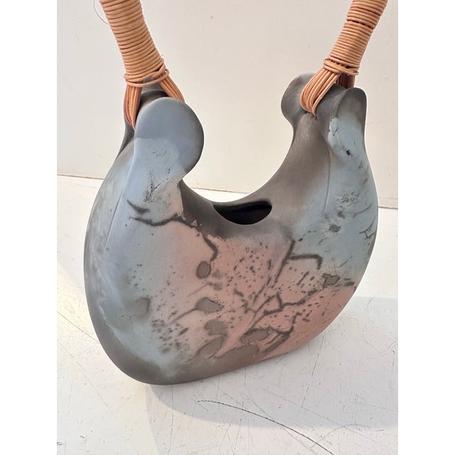 This distinctive raku‑style ceramic vessel features an organic, sculptural form with a smooth, smoke‑patterned surface...