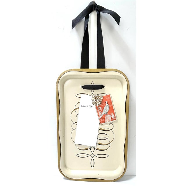 A versatile vintage mid-century metal tray featuring delicate pinstriped flourishes and a black grosgrain ribbon hanger....