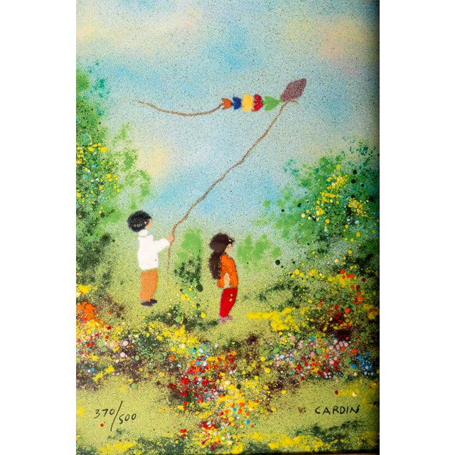 A joyful original enamel on copper by Louis Cardin depicting two children flying a kite amid a colorful flower-filled...