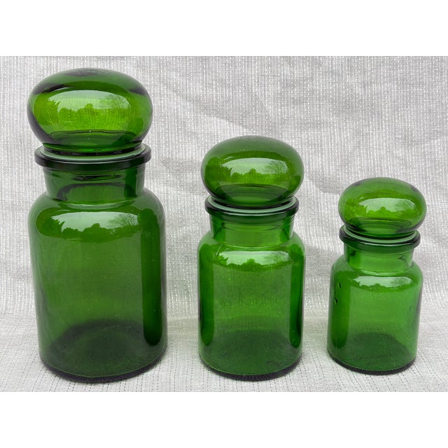 Vintage set of three green glass lidded apothecary jars. Small, medium and large. Bubble shaped lids with large plastic...