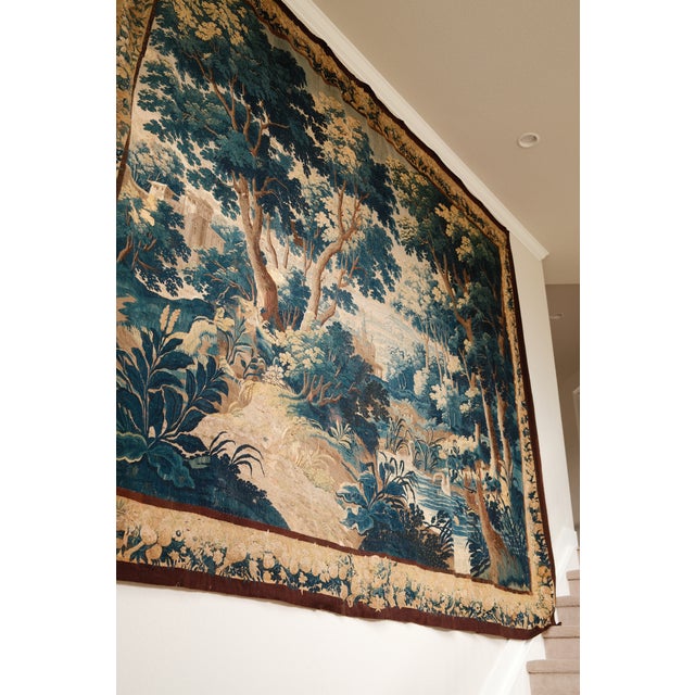 A massive handwoven verdure in the full 17th c. manner: a wooded river landscape with broad-leaved plants across the...