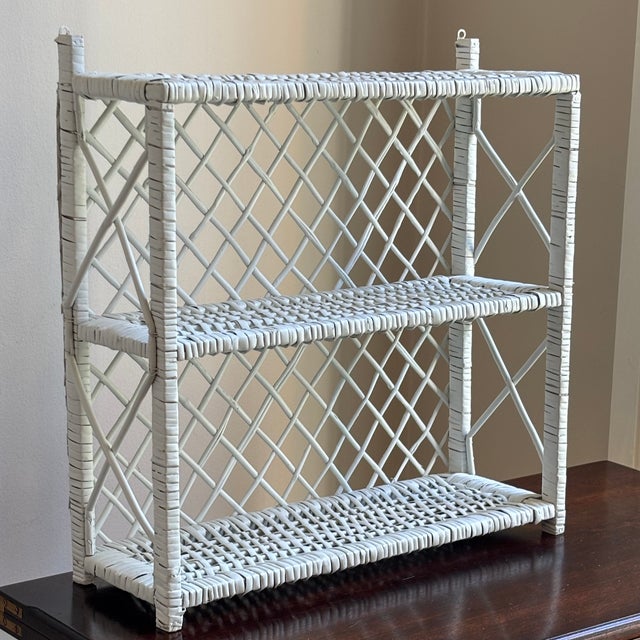 A charming vintage wicker wall shelf featuring an airy lattice design and crisp white-painted finish. Handcrafted from...