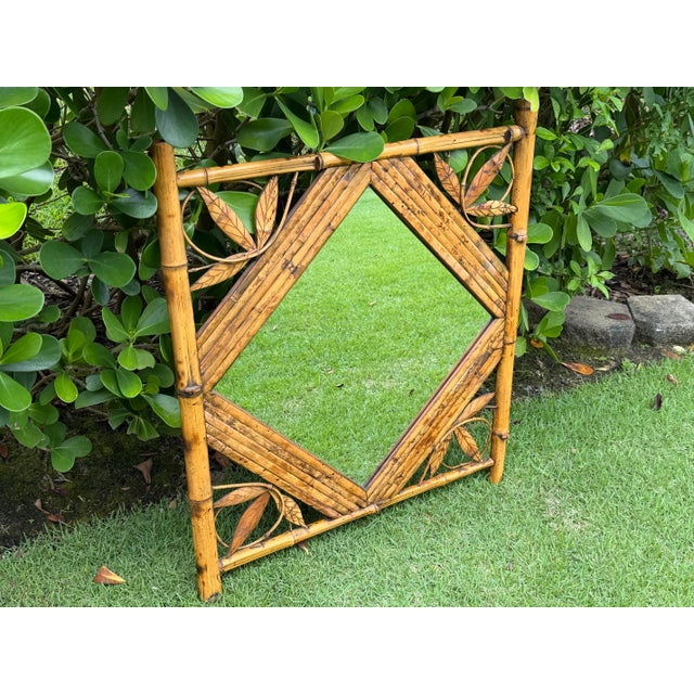 A charming vintage bamboo and rattan wall mirror featuring a diamond-form mirror plate framed by carved leaf details. The...