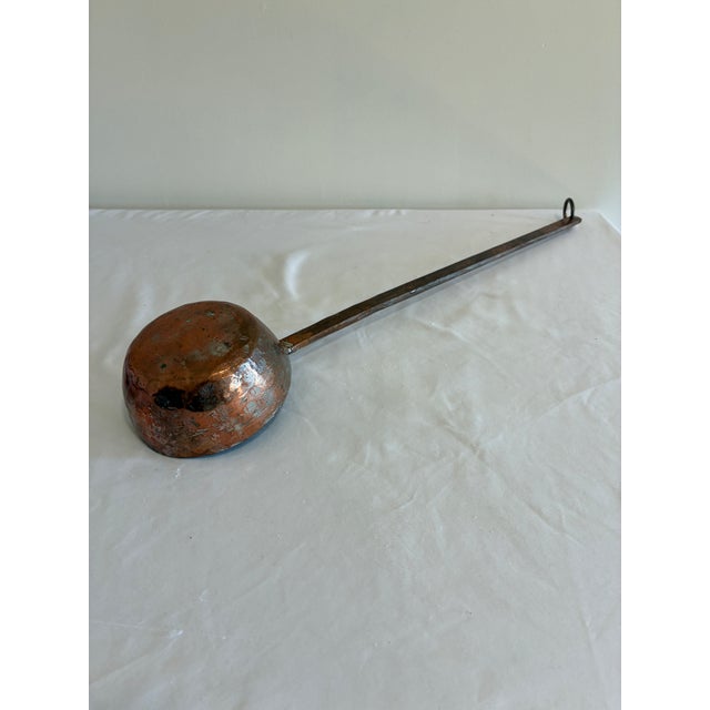 An antique copper ladle with a beautifully dimpled, hand-hammered bowl and rich aged patina, joined to a long forged iron...