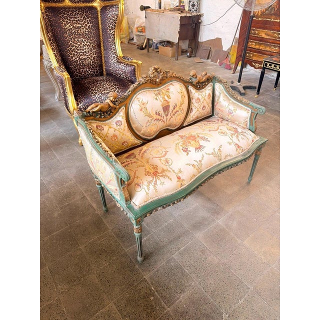 A charming French Louis XVI-style canapé settee featuring a carved sage-green wood frame, soft floral upholstery, and...
