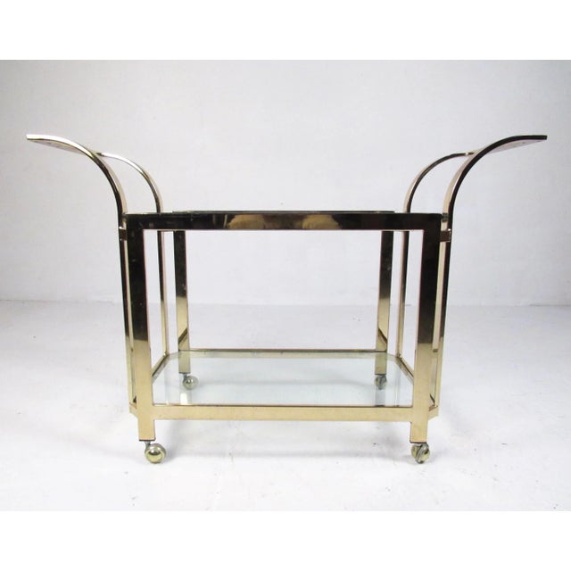 This two-tier brass finish service cart features unique modern design, shapely curved handles, and makes a striking bar...