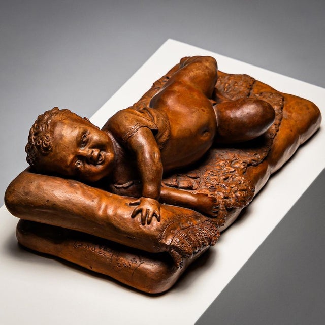 Small terracotta of a lying infant on fur and cushion with lace border. Signed at the head 23 No. \. 92, F. SANS.