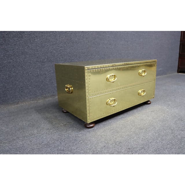 Brass clad two-drawer chest featuring an aviation-inspired riveted exterior, oval brass ring pulls, and dark wood bun...