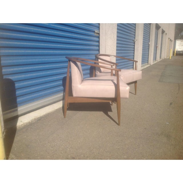Modern mid century lounge chairs done in a cream leather upholstery. The chairs have a walnut finish. The chairs are circa...