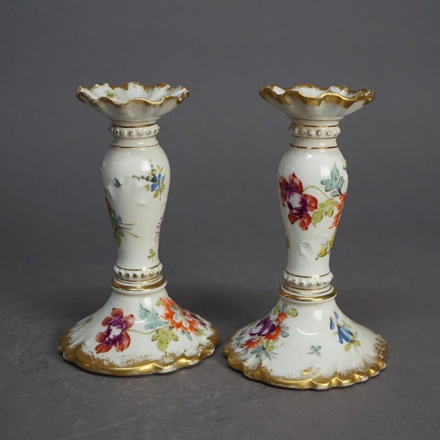 An antique German pair of candlesticks offer porcelain construction with hand painted floral decoration and gilt...