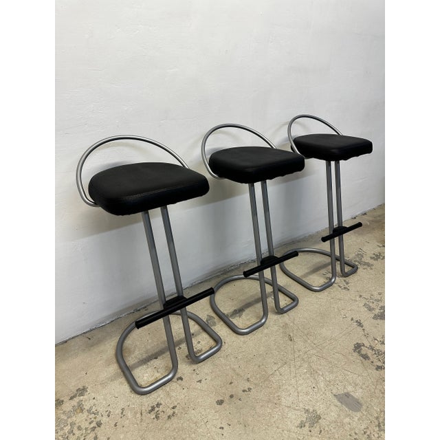 Set of three postmodern Italian barstools with black Naugahyde seats and silver lacquered frames with footrests.