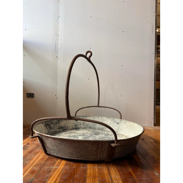 A heavy-duty industrial basin with a sturdy arched handle and hook. This is a raw, primitive farmhouse object with a...