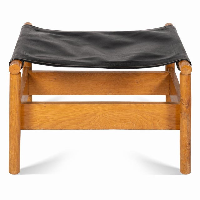 Wooden footstool, probably from the 1960s. It has a solid beech wood frame covered with firm black leather. The footstool...