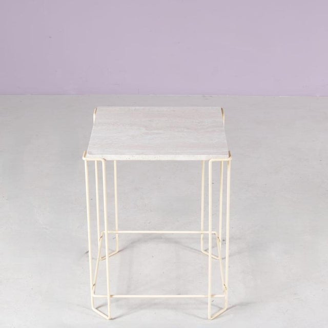 This 1980s side table combines a beige lacquered metal frame with a travertine stone top and is designed in the style of...