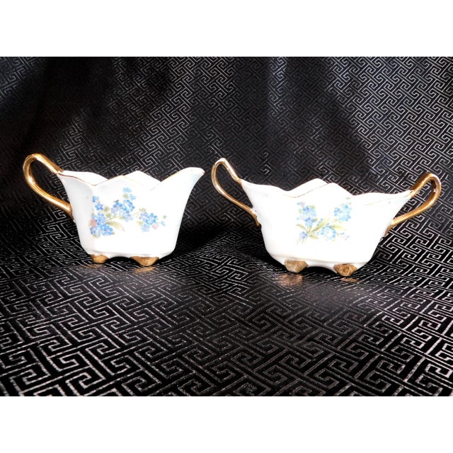 This is an unmarked and possibly hand painted white sugar bowl and creamer with a blue floral design. There are one or two...