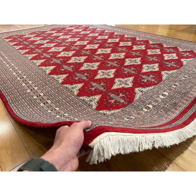 This is a Pakistani Bokhara Tekke rug, hand-knotted with wool. It features a rich red field covered with repeating Tekke...