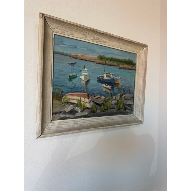 A charming 1970’s vintage oil on board landscape painting depicting a peaceful lakeside scene with several small boats...