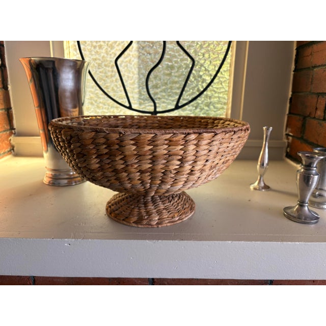 Sculptural vintage pedestal bowl handwoven from natural plant fibers in warm earthy brown tones. The wide, shallow bowl is...