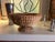 Sculptural vintage pedestal bowl handwoven from natural plant fibers in warm earthy brown tones. The wide, shallow bowl is...