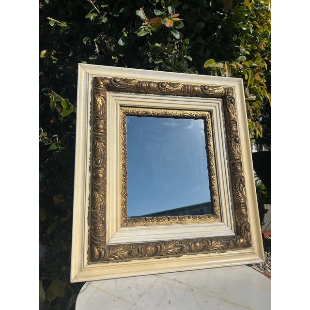 Vintage rectangular mirror featuring a layered wood frame with distressed cream finish and ornate gilt carved detailing....