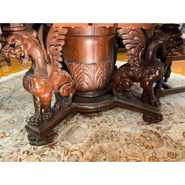 A striking, 60” round oak dining room table with a deep relief carved skirt and distinctive carved griffin legs in the...